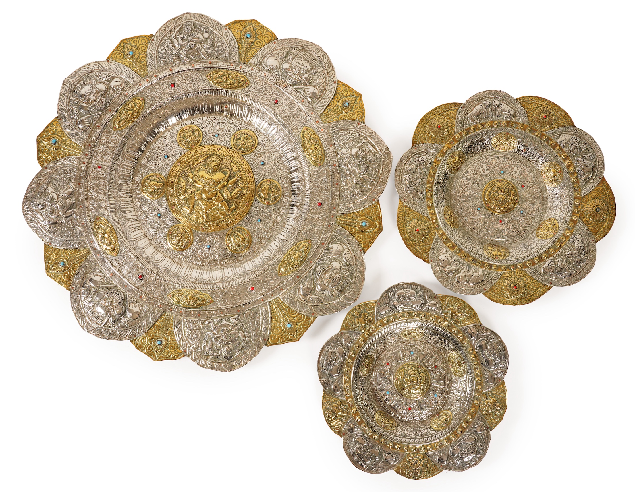 A graduated set of three Nepalese repoussé white metal and brass chargers, first half 20th century